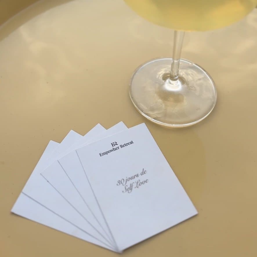 Les cartes du jeu 30 jours de Self Love, posées sur un plateau à côté d'un verre
